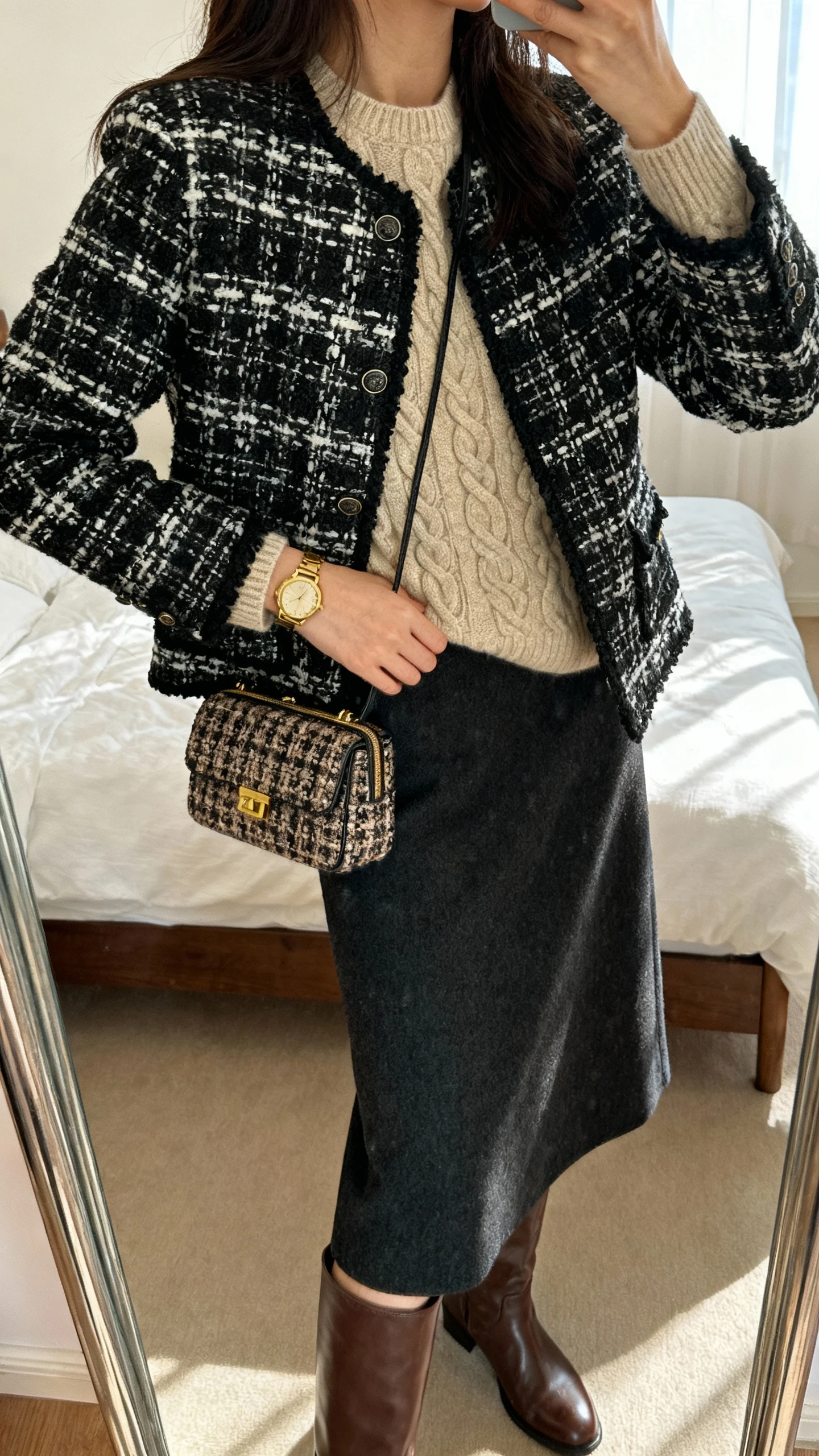 iPhone side-angle mirror selfie of a woman wearing a black-and-ivory tweed jacket over a beige cable-knit sweater, dark wool midi skirt, brown leather knee boots, vintage-inspired gold watch, and a structured tweed mini bag, face not visible, cropped at shoulders, bedroom mirror, soft afternoon light, iPhone photo quality.