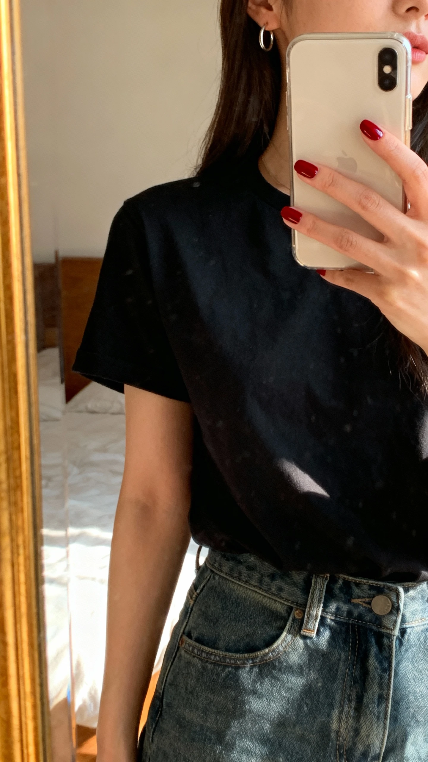 iPhone side-angle mirror selfie of a woman with monochrome pop nails (all nails one bold color like cherry red), wearing a black tee and high-waist jeans, small hoop earrings, face not visible, bedroom mirror, natural afternoon light, iPhone photo quality